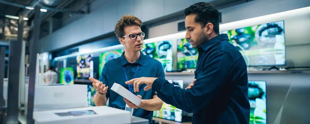 A man looking into buying a phone in a store and asking questions to an employee