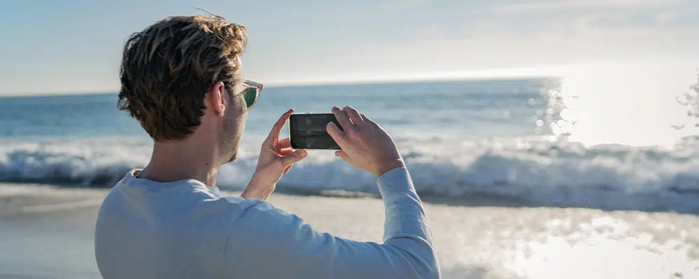 Man Holding Phone, Taking picture of beach sunset