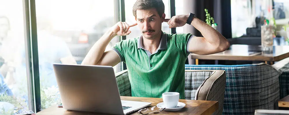 Man sitting in a cafe with his fingers in his ears so he cant hear