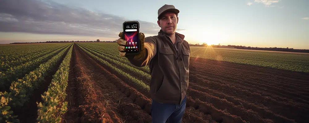 Farmer in farm field holding Kyocera Phone to camera