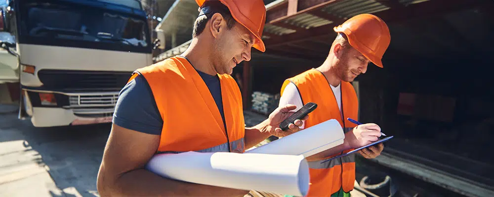 Two constructions workers looking at paperwork while holding kyocera phones