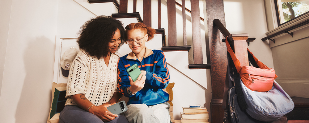 Two friends sitting together on staircase holding Pixel 9 and enjoying their time together