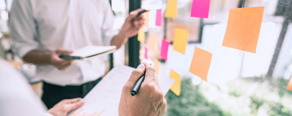 Two people planning by taking notes and looking at sticky notes on a glass wall