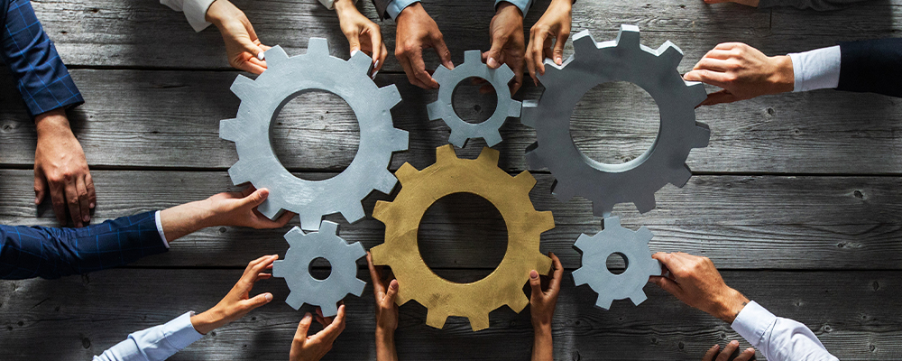 Group of business people joining together silver and golden colored gears on table at workplace top view